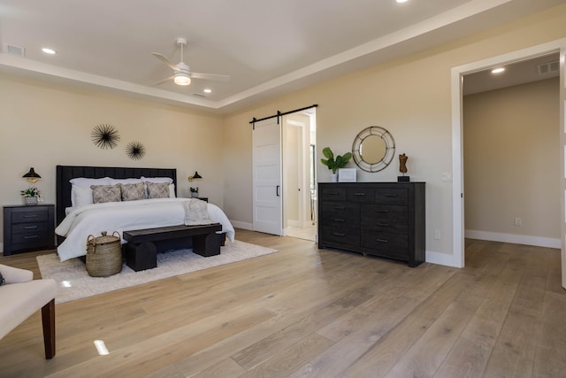 bedroom featuring ceiling fan, light wood-type flooring, and a barn door