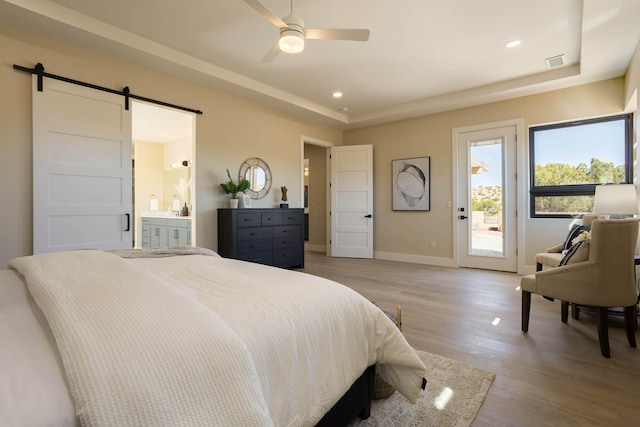 bedroom featuring light hardwood / wood-style floors, access to outside, a barn door, ensuite bathroom, and ceiling fan