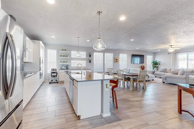 kitchen featuring white cabinets, ceiling fan, stainless steel appliances, and an island with sink