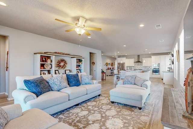 living room featuring ceiling fan, a textured ceiling, and light hardwood / wood-style floors