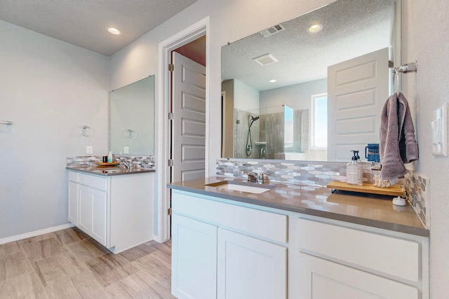 bathroom with vanity, an enclosed shower, a textured ceiling, and tasteful backsplash