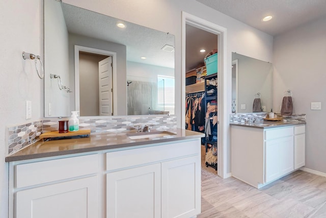 bathroom with vanity, a shower with shower door, a textured ceiling, and backsplash