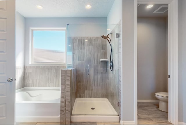 bathroom with toilet, a textured ceiling, shower with separate bathtub, and hardwood / wood-style floors