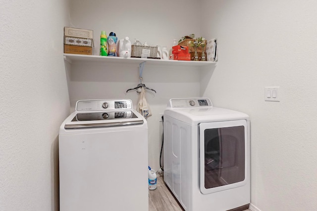 laundry room with washing machine and clothes dryer and light wood-type flooring