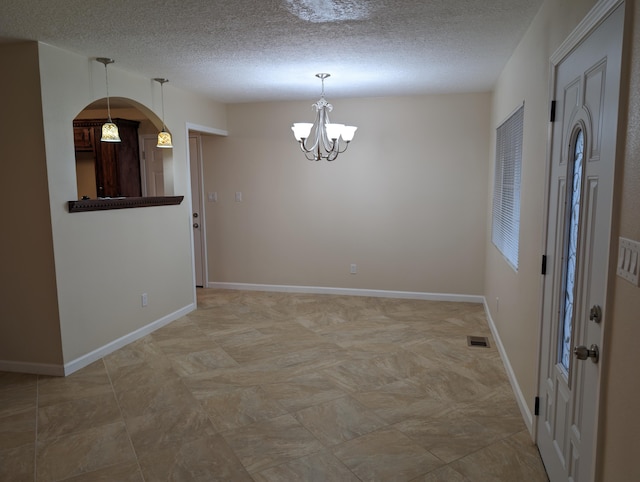 empty room featuring a textured ceiling and a chandelier