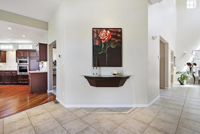 hall with light tile patterned floors, recessed lighting, a high ceiling, and baseboards