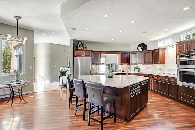 kitchen featuring wood finished floors, a large island with sink, decorative backsplash, light countertops, and a kitchen bar