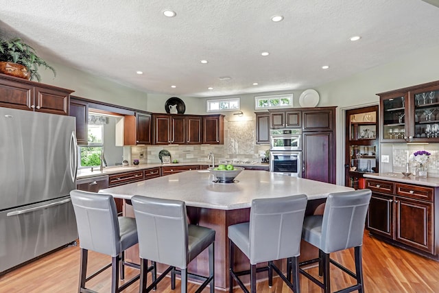 kitchen with an island with sink, light countertops, a kitchen breakfast bar, light wood-style floors, and stainless steel appliances