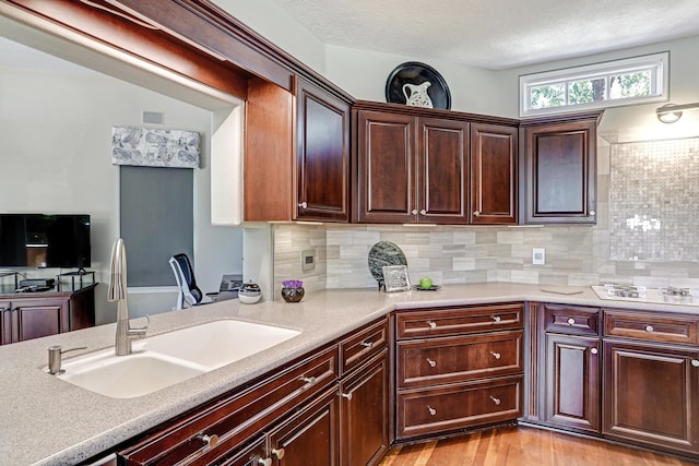 kitchen with a sink, light countertops, a textured ceiling, tasteful backsplash, and light wood-type flooring