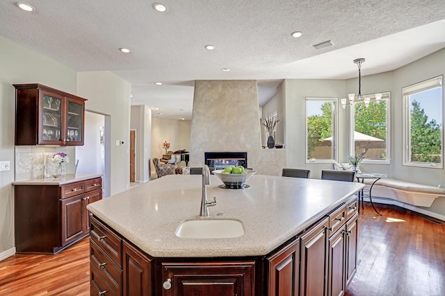 kitchen with visible vents, a sink, a fireplace, light wood finished floors, and decorative backsplash