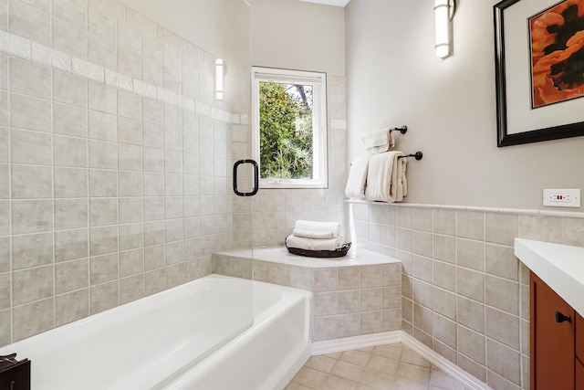 full bathroom with tile patterned floors, a wainscoted wall, vanity, a bath, and tile walls