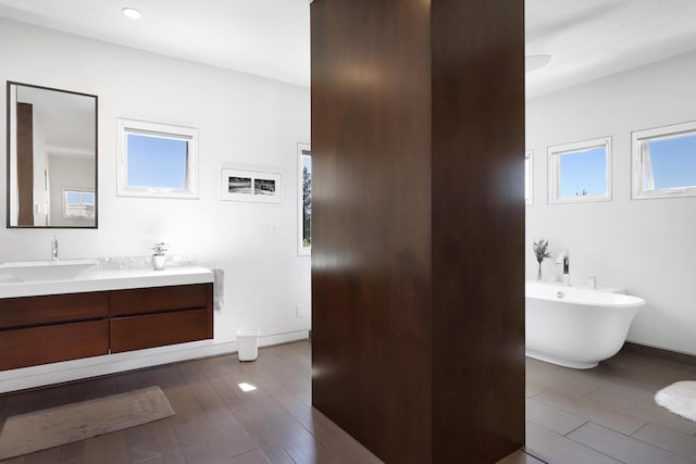 bathroom with a soaking tub, vanity, baseboards, and wood finished floors