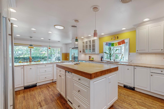 kitchen featuring a wealth of natural light, white cabinetry, a center island with sink, and decorative light fixtures