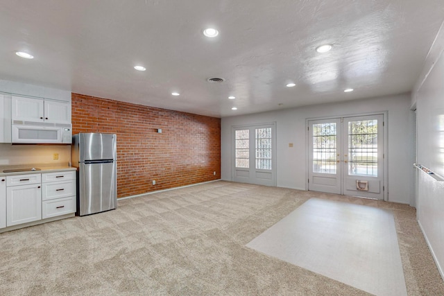 kitchen with stainless steel fridge, brick wall, light colored carpet, and white cabinets