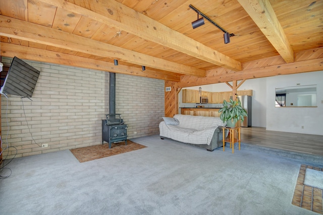 unfurnished living room featuring beamed ceiling, track lighting, a wood stove, and brick wall