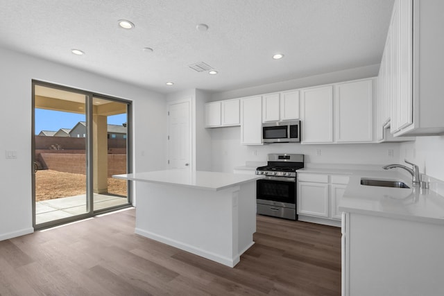 kitchen featuring dark wood-style floors, a sink, appliances with stainless steel finishes, white cabinetry, and a center island