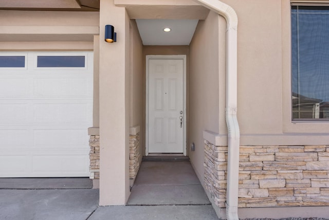 entrance to property featuring stone siding, stucco siding, and a garage