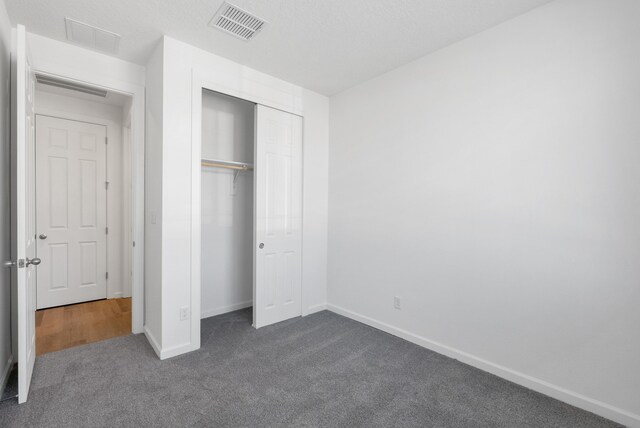 unfurnished bedroom with a closet, visible vents, baseboards, and dark colored carpet