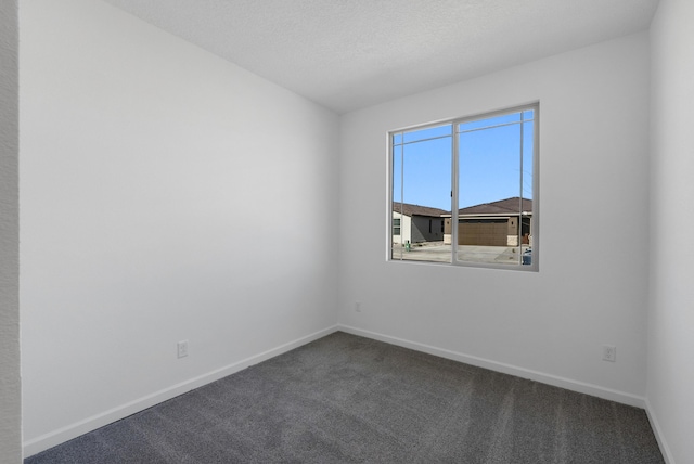 spare room with dark colored carpet, baseboards, and a textured ceiling