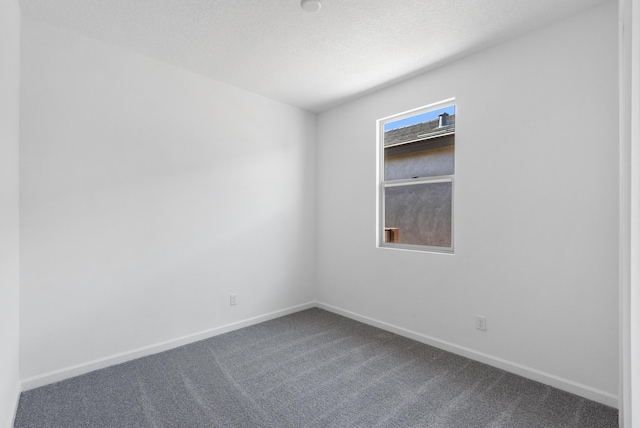 spare room featuring dark carpet, a textured ceiling, and baseboards