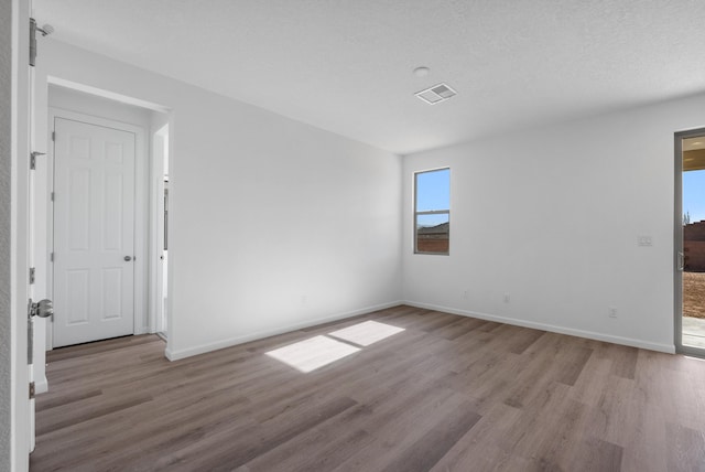 unfurnished room with visible vents, a textured ceiling, baseboards, and wood finished floors