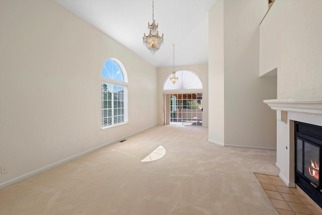 unfurnished living room featuring light colored carpet, a notable chandelier, plenty of natural light, and high vaulted ceiling