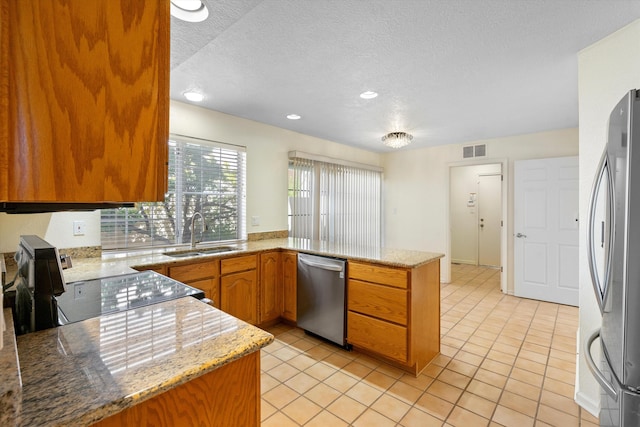 kitchen with light stone counters, kitchen peninsula, stainless steel appliances, a textured ceiling, and sink