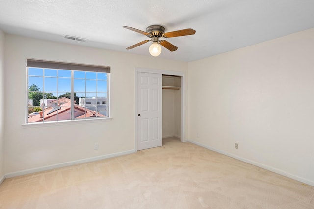 unfurnished bedroom featuring ceiling fan, light colored carpet, and a closet