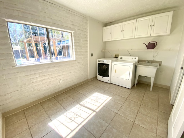 laundry room featuring washer and dryer, cabinets, brick wall, and light tile patterned floors