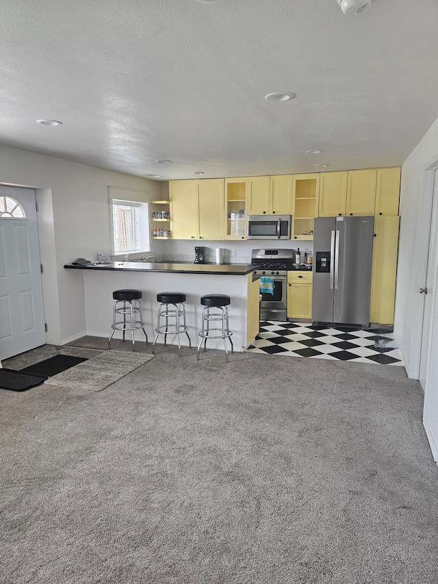 kitchen with dark colored carpet, a textured ceiling, kitchen peninsula, a kitchen breakfast bar, and appliances with stainless steel finishes