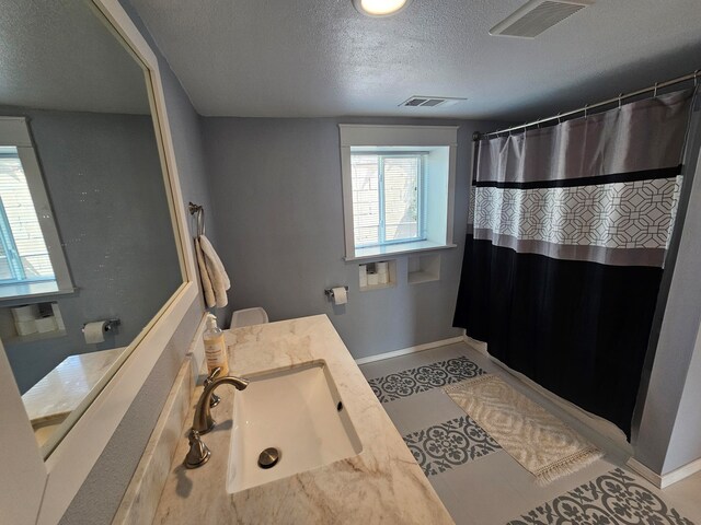 bathroom with a textured ceiling, toilet, vanity, and curtained shower