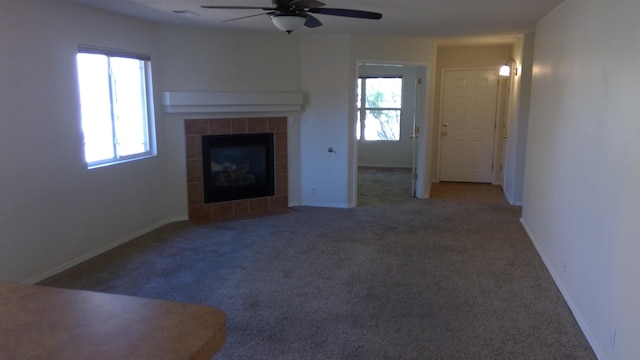 unfurnished living room with carpet floors, a tiled fireplace, ceiling fan, and a wealth of natural light