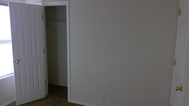 unfurnished bedroom with a closet and dark colored carpet