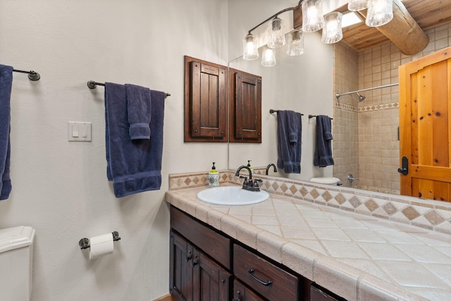 bathroom with a tile shower, vanity, and toilet