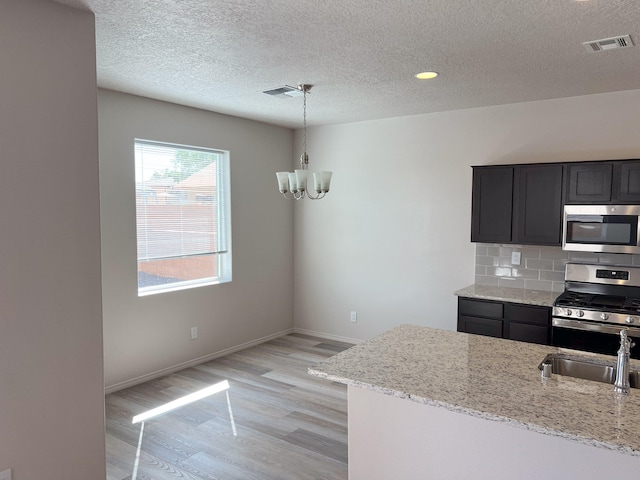 kitchen featuring appliances with stainless steel finishes, decorative backsplash, light hardwood / wood-style floors, light stone countertops, and decorative light fixtures