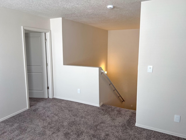 spare room featuring a textured ceiling and dark colored carpet