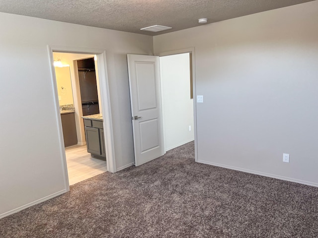 unfurnished bedroom featuring a textured ceiling, ensuite bath, and light colored carpet