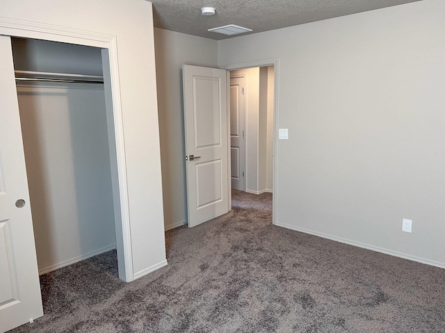 unfurnished bedroom featuring a textured ceiling, a closet, and dark colored carpet