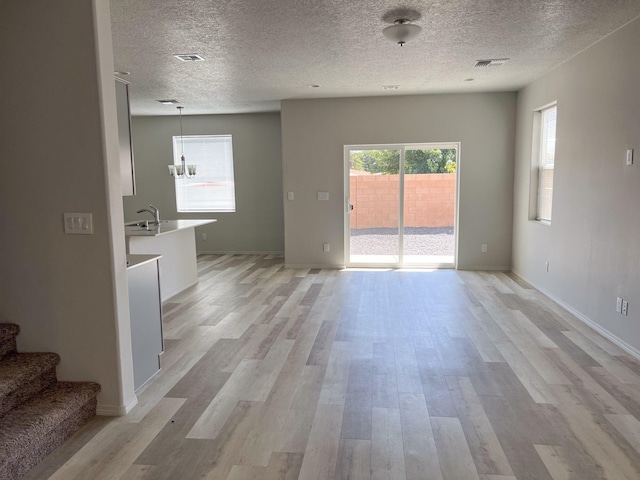 unfurnished living room with a textured ceiling, light hardwood / wood-style floors, and a notable chandelier