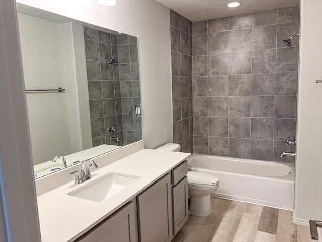 full bathroom with vanity, a textured ceiling, wood-type flooring, tiled shower / bath combo, and toilet