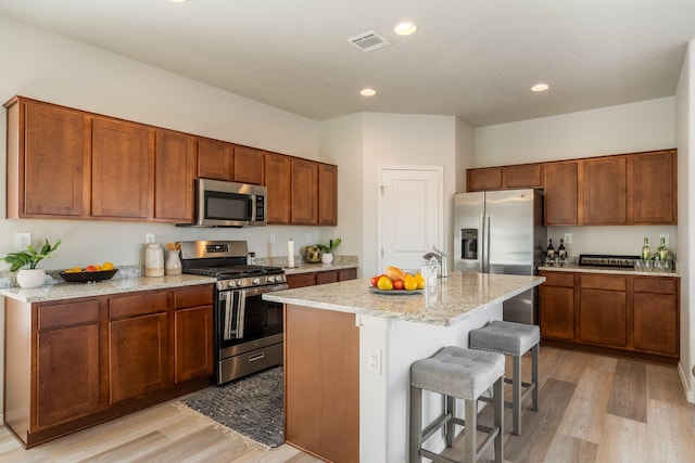 kitchen featuring light wood-type flooring, an island with sink, a kitchen bar, appliances with stainless steel finishes, and light stone countertops