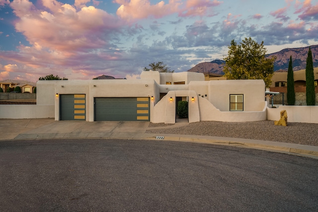 pueblo-style home featuring concrete driveway, an attached garage, fence, a mountain view, and stucco siding