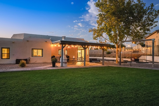 back of house at dusk featuring a yard, a patio, fence, and stucco siding