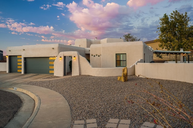 southwest-style home featuring a garage, concrete driveway, fence, and stucco siding