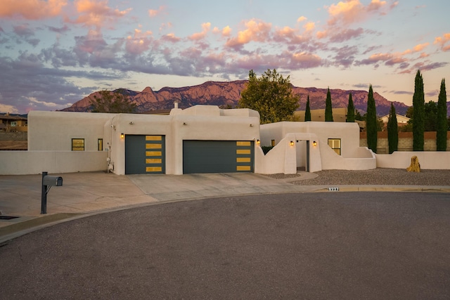 pueblo-style home featuring stucco siding, fence, a mountain view, a garage, and driveway