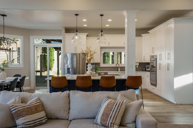 living area with ornate columns, recessed lighting, and light wood-style floors