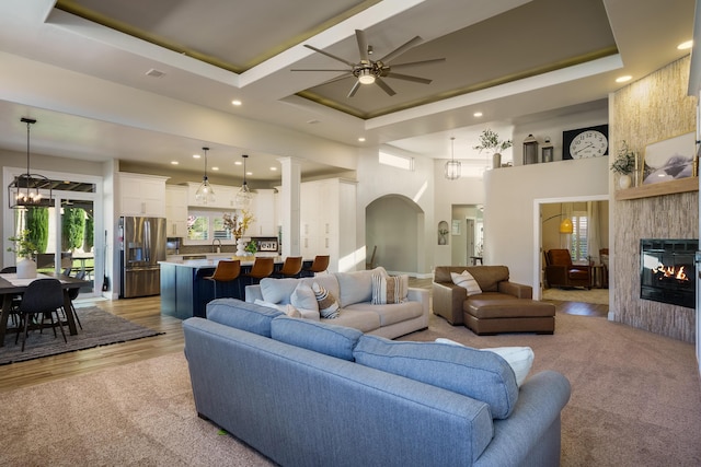 living room featuring a towering ceiling, a tray ceiling, and a glass covered fireplace