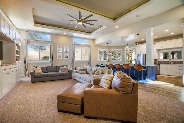 living area featuring a tray ceiling, ceiling fan, decorative columns, and recessed lighting