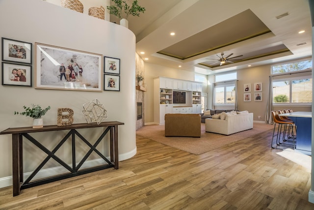 living room featuring baseboards, a raised ceiling, ceiling fan, light wood-style floors, and recessed lighting