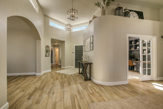 foyer with arched walkways, light wood finished floors, a high ceiling, and baseboards